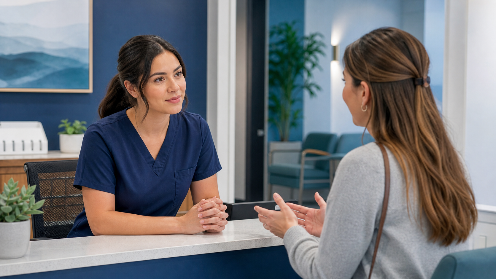 Two healthcare workplace professionals using attentive listening and open posture during a front-desk conversation.